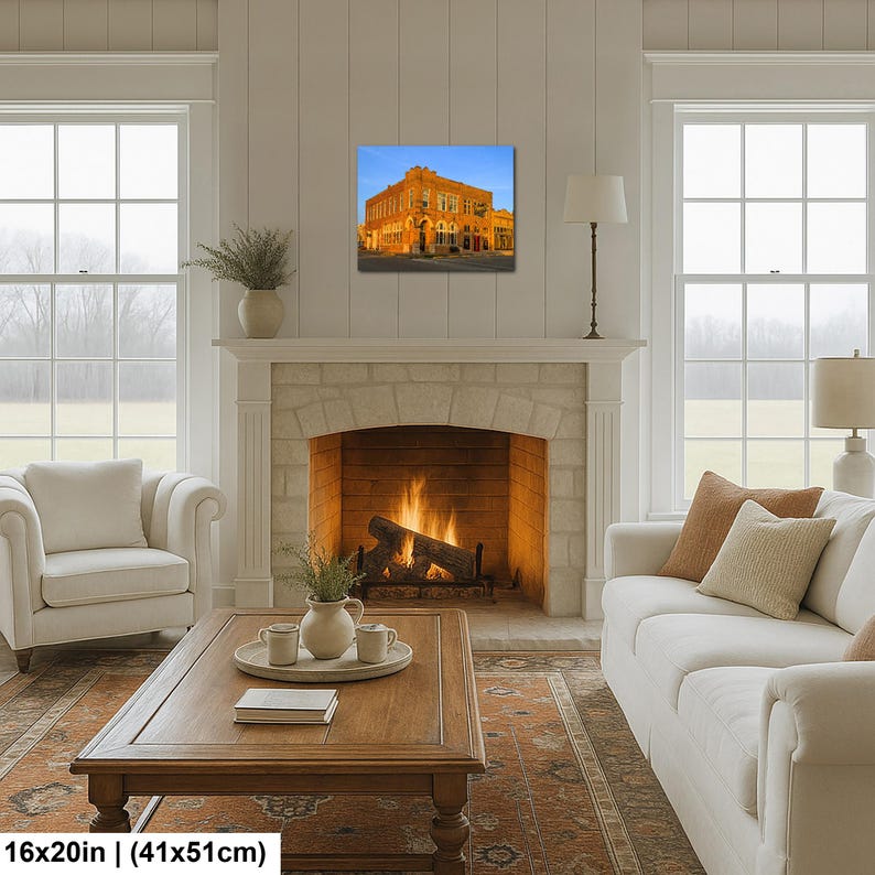 May include: A rectangular wall art print measuring 16 inches by 20 inches, featuring a warm-toned, multi-story brick building illuminated at dusk against a clear blue sky, displayed in a living room above a stone fireplace mantel.