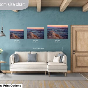 May include: A living room size chart displaying three landscape canvas prints of a desert canyon at sunset, sized 16x24 inches, 20x30 inches, and 24x36 inches, positioned above a cream-colored sectional sofa with gray throw pillows.
