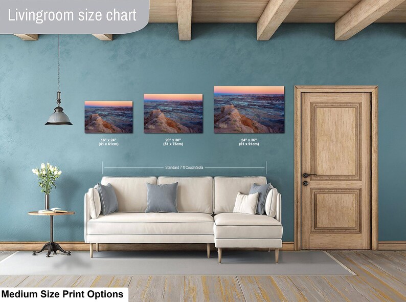 May include: A living room size chart displaying three landscape canvas prints of a desert canyon at sunset, sized 16x24 inches, 20x30 inches, and 24x36 inches, positioned above a cream-colored sectional sofa with gray throw pillows.