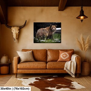 May include: A rectangular wall art print featuring a brown bear standing in a snowy forest, displayed above a brown leather sofa with two throw pillows, a white blanket, a cowhide rug, and a skull mount on the wall. Dimensions: 76x102 cm.
