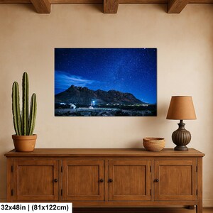 Puede incluir: Una impresi&oacute;n de arte mural rectangular que mide 81 por 122 cm, con un paisaje nocturno de una cadena monta&ntilde;osa oscura bajo un cielo estrellado azul profundo. La escena incluye una peque&ntilde;a estructura iluminada al pie de las monta&ntilde;as.