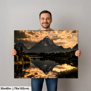 Puede incluir: Un cuadro de paisaje rectangular que mide 76 por 102 cm, con una cordillera reflejada en un lago tranquilo al atardecer. El cielo est&aacute; lleno de nubes doradas iluminadas sobre las siluetas oscuras de los &aacute;rboles y los picos escarpados.