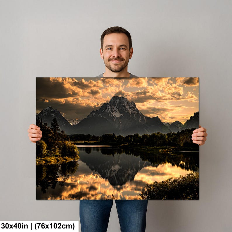 Puede incluir: Un cuadro de paisaje rectangular que mide 76 por 102 cm, con una cordillera reflejada en un lago tranquilo al atardecer. El cielo est&aacute; lleno de nubes doradas iluminadas sobre las siluetas oscuras de los &aacute;rboles y los picos escarpados.