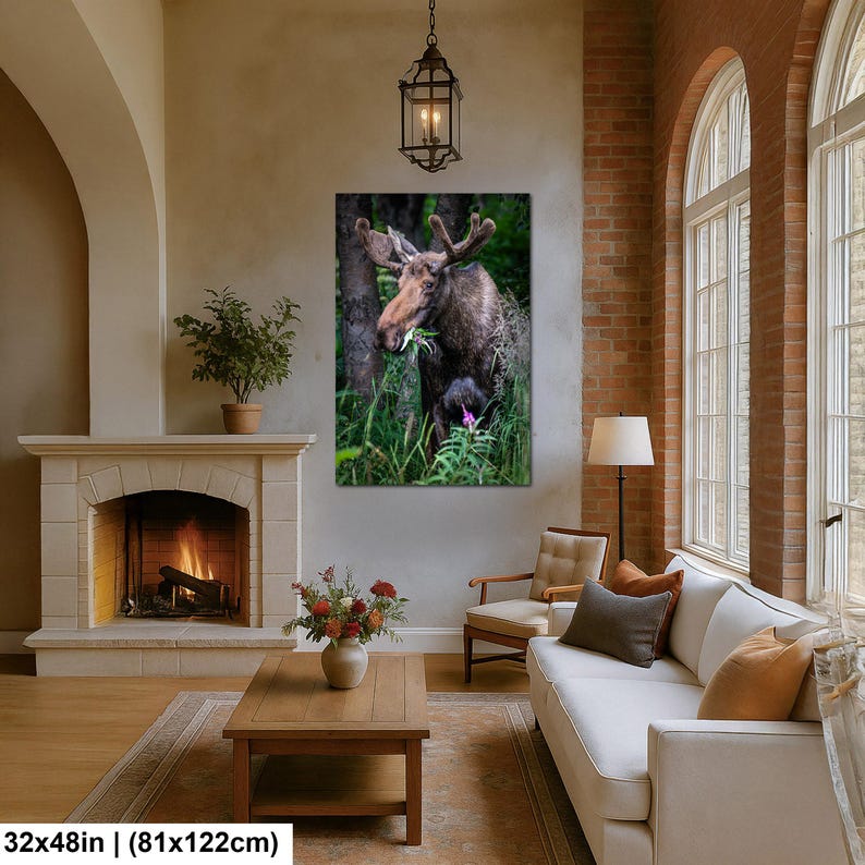 May include: A rectangular wall art print featuring a brown moose with large antlers standing in a lush green forest, eating foliage. The print is displayed in a living room above a fireplace, with dimensions of 32 inches by 48 inches.