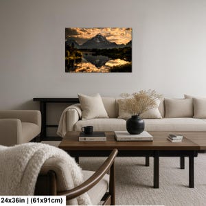 Puede incluir: Un cuadro rectangular de pared que muestra un paisaje monta&ntilde;oso al atardecer con nubes doradas reflejadas en un lago tranquilo. La impresi&oacute;n mide 61 cm por 91 cm y se exhibe en una pared gris claro sobre un sof&aacute; beige y una mesa de madera.