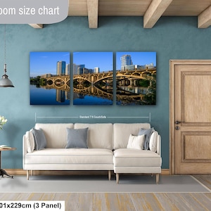 May include: A three-panel wall art set depicting a city skyline and bridge over water, displayed above a white sectional sofa. The text Livingroom size chart is visible at the top, with 40x90in | 101x229cm (3 Panel) at the bottom.