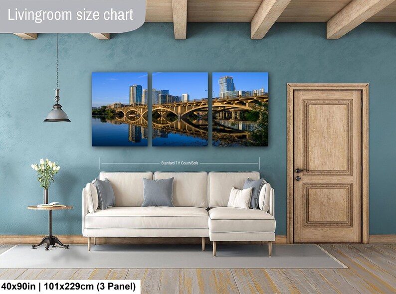 May include: A three-panel wall art set depicting a city skyline and bridge over water, displayed above a white sectional sofa. The text Livingroom size chart is visible at the top, with 40x90in | 101x229cm (3 Panel) at the bottom.