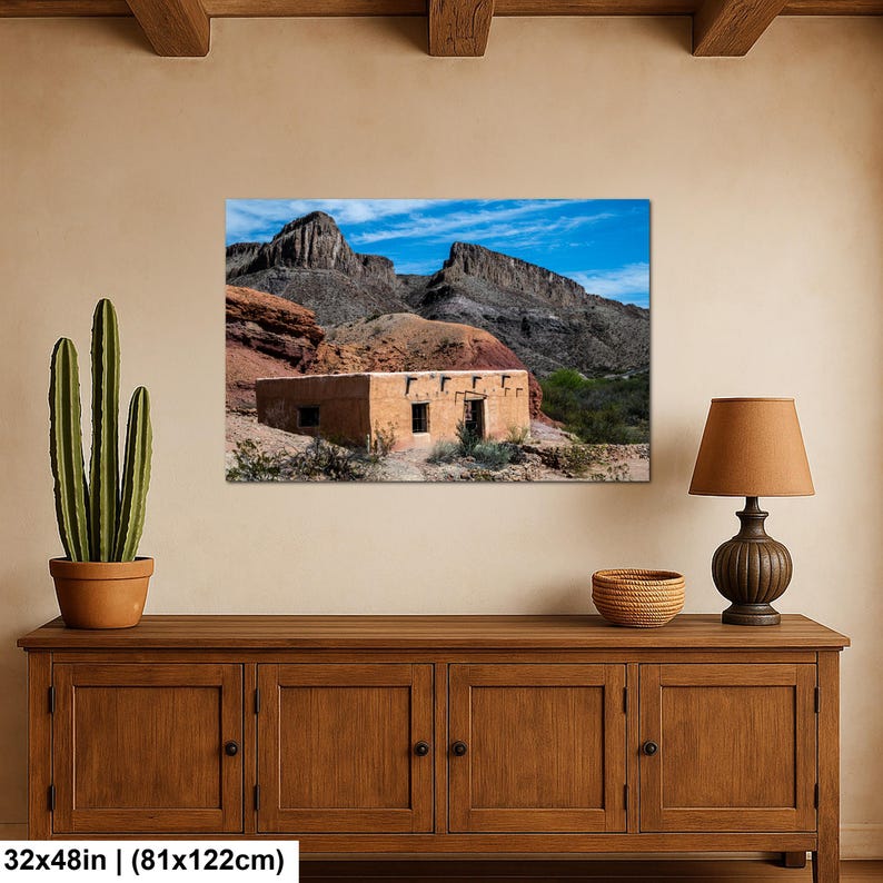 May include: A rectangular wall art print measuring 32 inches by 48 inches, depicting a tan adobe building situated in a desert landscape with rocky mountains under a blue sky. The print is displayed on a wall above a wooden cabinet.