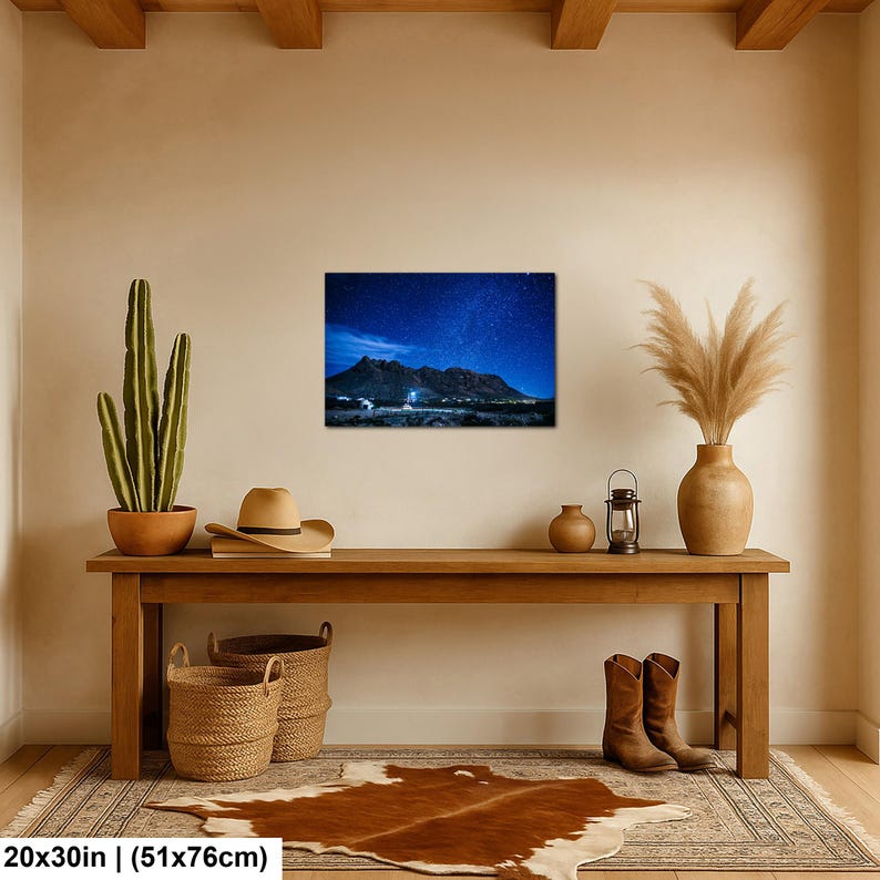 Puede incluir: Una impresi&oacute;n de arte mural rectangular que muestra un paisaje nocturno con un cielo estrellado azul oscuro sobre una cadena monta&ntilde;osa y un horizonte des&eacute;rtico. La impresi&oacute;n mide 51 por 76 cm y se exhibe en una pared de color beige.