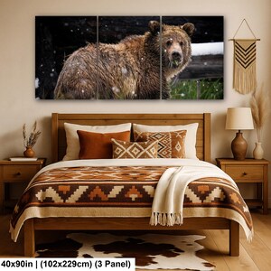 May include: A three-panel wall art set depicting a brown bear in a snowy forest, displayed above a wooden bed frame with a patterned brown and cream quilt, two orange pillows, and a cream throw blanket, measuring 102 by 229 cm.