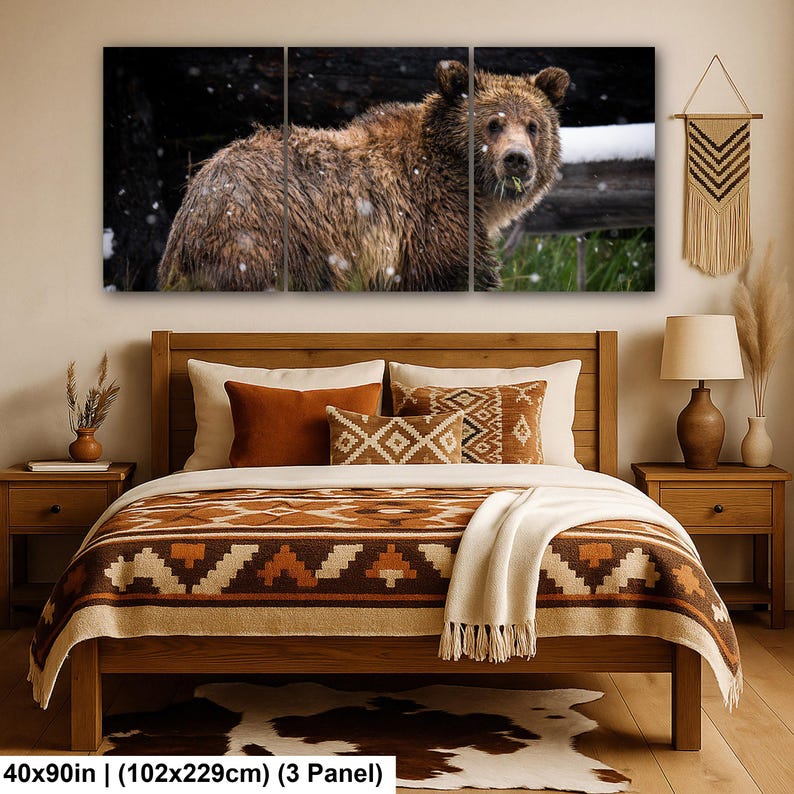 May include: A three-panel wall art set depicting a brown bear in a snowy forest, displayed above a wooden bed frame with a patterned brown and cream quilt, two orange pillows, and a cream throw blanket, measuring 102 by 229 cm.