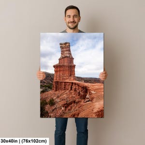 May include: A rectangular wall art print measuring 30 by 40 inches, featuring a high-resolution landscape photograph of a tall, reddish-brown rock formation rising from a desert canyon floor under a cloudy sky with visible rocky terrain.
