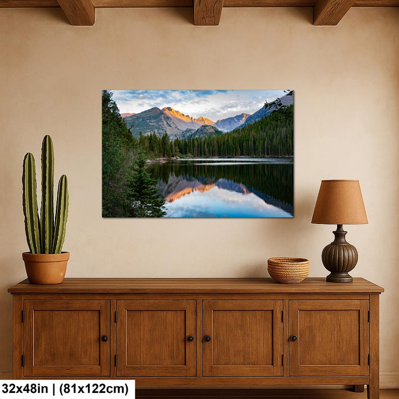 May include: A rectangular wall art print measuring 32 by 48 inches, featuring a landscape photograph of a calm lake reflecting snow-capped mountain peaks at sunrise, surrounded by a dense forest of green pine trees under a blue sky.