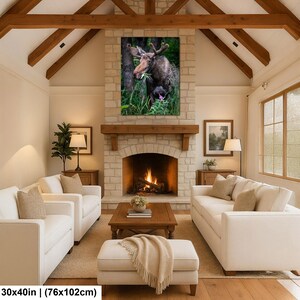 May include: A rectangular wall art print featuring a brown moose standing in a lush green forest, eating foliage. The artwork is displayed above a stone fireplace in a living room. The print measures 30 inches by 40 inches in total size.