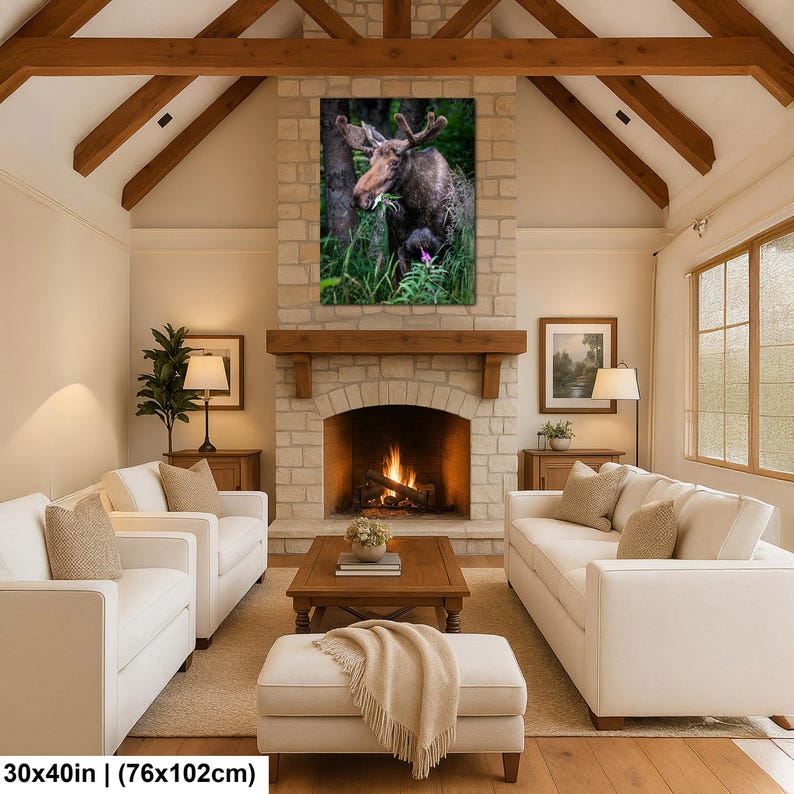 May include: A rectangular wall art print featuring a brown moose standing in a lush green forest, eating foliage. The artwork is displayed above a stone fireplace in a living room. The print measures 30 inches by 40 inches in total size.