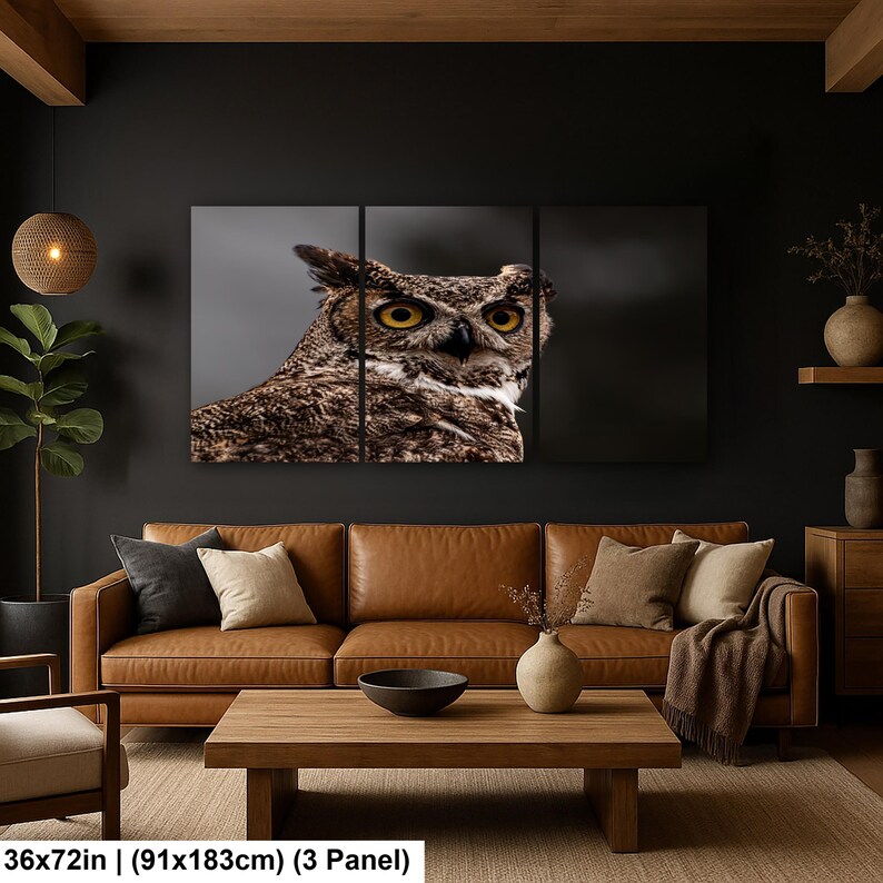 May include: A three-panel wall art set featuring a close-up photograph of a great horned owl with yellow eyes and brown patterned feathers. The artwork measures 36 by 72 inches and is displayed as a triptych on a dark wall above a leather sofa.