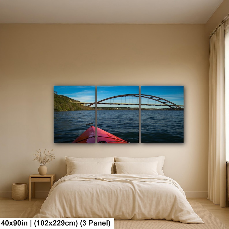 May include: A three-panel wall art set depicting a red kayak bow on dark blue water facing a large arched bridge under a clear blue sky. The artwork measures 40 by 90 inches and features a landscape view of a river scene with a bridge span.
