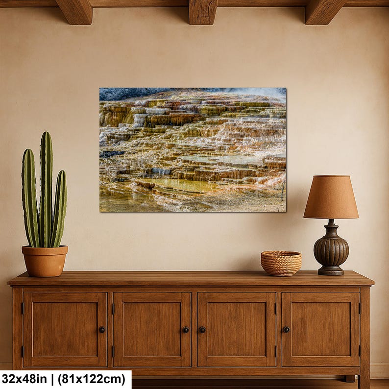 May include: A rectangular wall art print featuring a landscape of layered mineral terraces with shades of orange, brown, and white. The artwork measures 32 inches by 48 inches and is displayed on a wall above a wooden cabinet with a cactus and lamp.