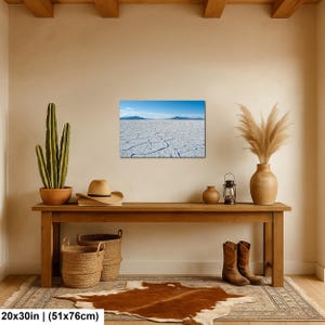 May include: A rectangular wall art print measuring 20 by 30 inches, featuring a landscape photograph of a white salt flat with cracked ground under a clear blue sky and distant mountains, displayed in a room with decor items.