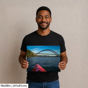 May include: A rectangular wall art print measuring 16 inches by 20 inches, featuring a landscape photograph of a red kayak bow in the foreground on a body of water, with a large arched bridge spanning across the background under a blue sky.