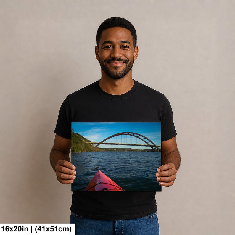 May include: A rectangular wall art print measuring 16 inches by 20 inches, featuring a landscape photograph of a red kayak bow in the foreground on a body of water, with a large arched bridge spanning across the background under a blue sky.