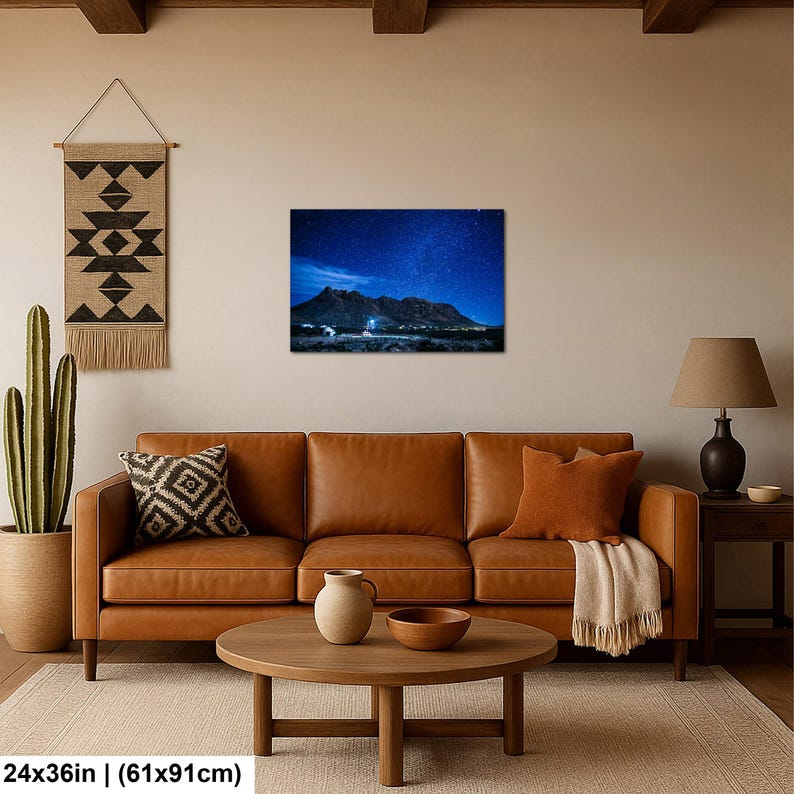 Puede incluir: Una impresi&oacute;n de arte mural rectangular que muestra un paisaje nocturno con un cielo estrellado azul oscuro sobre una cadena monta&ntilde;osa. La impresi&oacute;n mide 61 cm por 91 cm y se muestra en una pared sobre un sof&aacute; de cuero marr&oacute;n y una mesa de centro.
