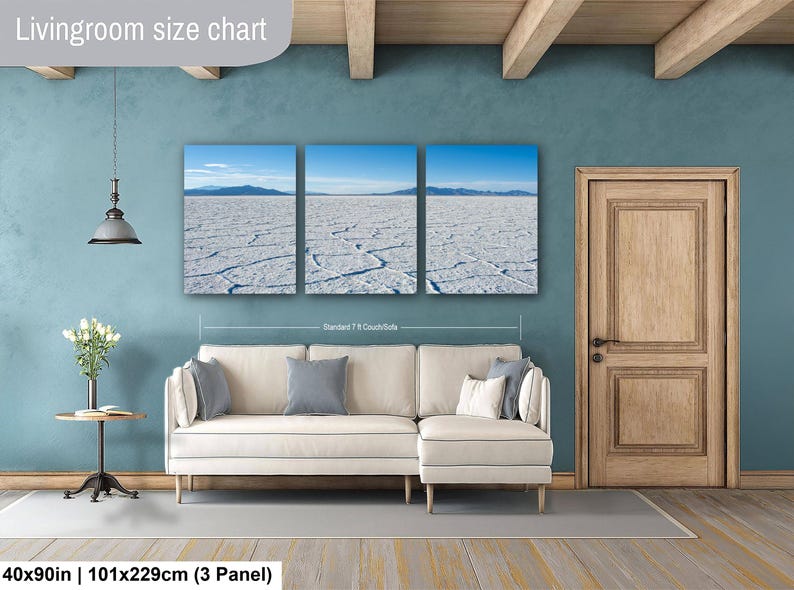 May include: A three-panel canvas wall art set depicting a white salt flat landscape under a blue sky, displayed above a cream-colored sectional sofa. The text Livingroom size chart and 40x90in | 101x229cm (3 Panel) is visible on the image.