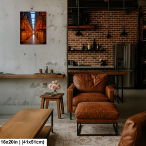 May include: A rectangular wall art print featuring a perspective view of a long, industrial corridor with glowing orange lights and metal structures. The artwork is displayed on a textured wall above a wooden side table with a vase of pink flowers.