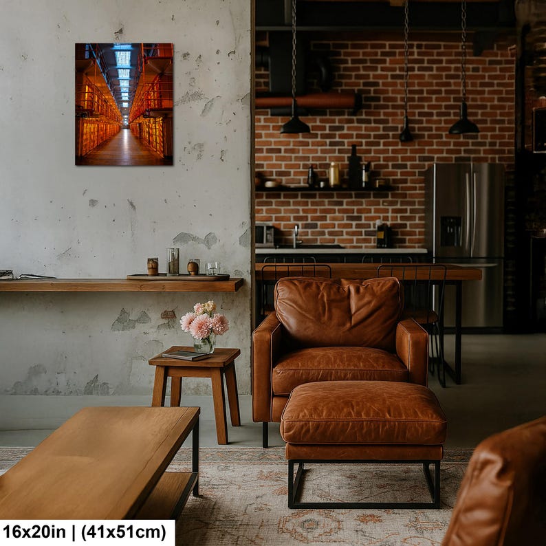 May include: A rectangular wall art print featuring a perspective view of a long, industrial corridor with glowing orange lights and metal structures. The artwork is displayed on a textured wall above a wooden side table with a vase of pink flowers.