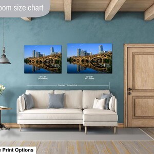 May include: A living room size chart displaying two rectangular wall art prints of a city skyline and bridge over water. The prints are labeled with dimensions of 30 x 40 inches and 32 x 48 inches, positioned above a white sectional sofa.