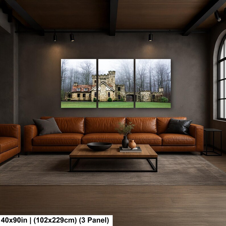 Op de afbeelding: Een driedelige wanddecoratieset met een stenen kasteel met een rood dak, omringd door een groen gazon en een mistig bos. De totale afmetingen van het kunstwerk zijn 102 bij 229 cm, gepresenteerd als een drieluik aan een donkere muur.