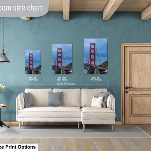 May include: A living room size chart displaying three vertical wall art prints of the Golden Gate Bridge in sizes 16 x 24 inches, 20 x 30 inches, and 24 x 36 inches, positioned above a cream-colored sectional sofa with gray and white throw pillows.