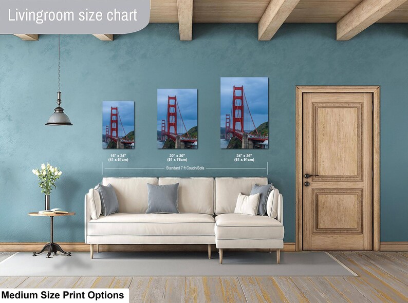 May include: A living room size chart displaying three vertical wall art prints of the Golden Gate Bridge in sizes 16 x 24 inches, 20 x 30 inches, and 24 x 36 inches, positioned above a cream-colored sectional sofa with gray and white throw pillows.