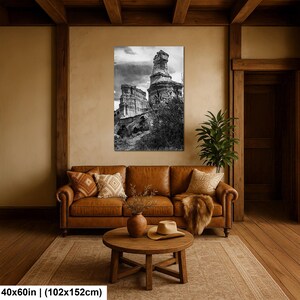May include: A black and white wall art print depicting a tall, weathered rock formation under a cloudy sky, measuring 40 by 60 inches. The artwork is displayed in a room with a brown leather sofa, a wooden coffee table, and a beige rug.