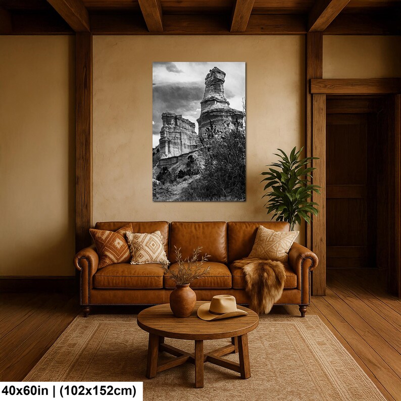 May include: A black and white wall art print depicting a tall, weathered rock formation under a cloudy sky, measuring 40 by 60 inches. The artwork is displayed in a room with a brown leather sofa, a wooden coffee table, and a beige rug.