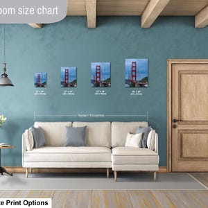 May include: A living room size chart displaying four framed prints of the Golden Gate Bridge in sizes 8x10, 11x14, 12x18, and 16x20 inches, positioned above a cream-colored sectional sofa. The text reads Livingroom size chart and Standard 7 ft Couch/Sofa.