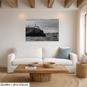 May include: A black and white landscape wall art print featuring a lighthouse perched on a rocky cliff overlooking the ocean under a cloudy sky. The artwork measures 32 inches by 48 inches and is displayed above a white sofa in a living room.