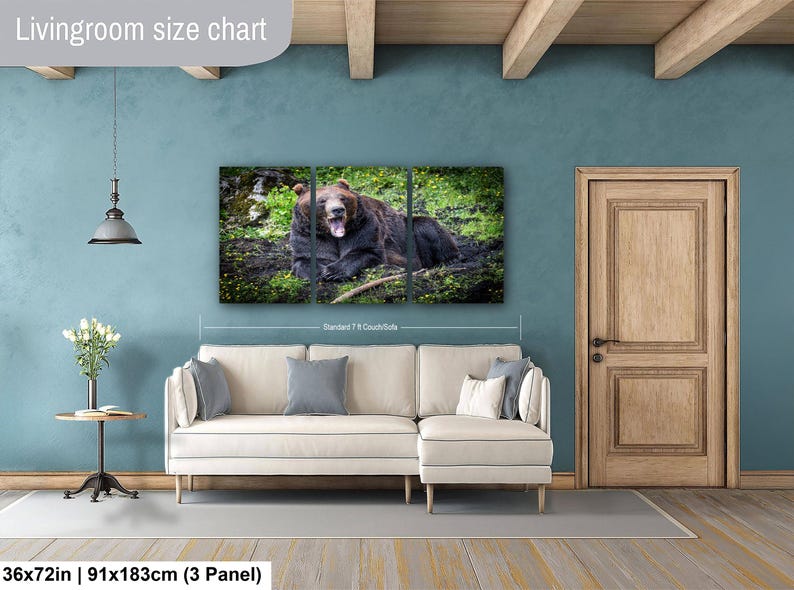May include: A three-panel wall art set featuring a brown bear resting in a grassy field, displayed above a cream-colored sectional sofa. The artwork measures 36 by 72 inches and is positioned to show scale relative to a standard 7-foot couch.