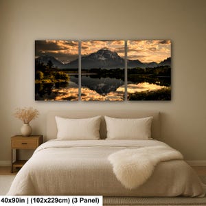 Puede incluir: Un conjunto de arte mural de tres paneles que representa una cordillera al atardecer reflejada en un lago tranquilo. El paisaje presenta siluetas oscuras de &aacute;rboles y monta&ntilde;as contra un cielo dorado y nublado. Las dimensiones totales son 102 cm por 229 cm.
