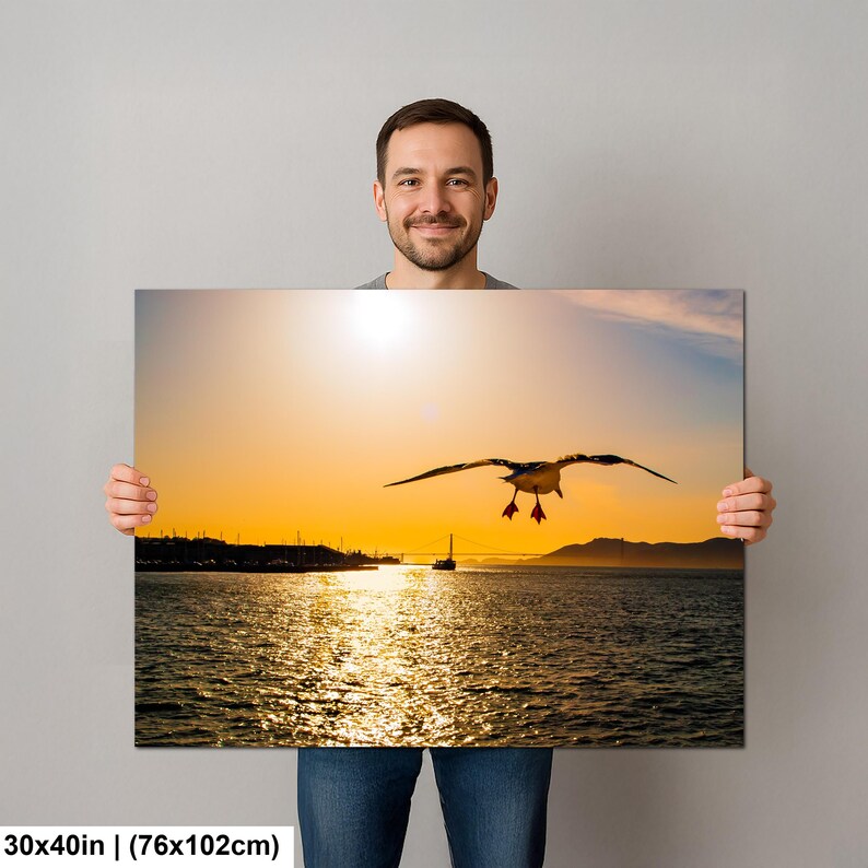 May include: A rectangular wall art print measuring 30x40 inches featuring a sunset over a body of water. A seagull is captured in flight in the center against a bright orange sky. A distant bridge silhouette is visible on the horizon line.