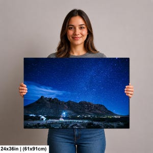 Puede incluir: Una impresi&oacute;n de arte mural rectangular que mide 61x91cm, con un paisaje nocturno de una cadena monta&ntilde;osa oscura bajo un cielo estrellado azul profundo. Una peque&ntilde;a estructura iluminada se encuentra en la base de las monta&ntilde;as, contrastando con el terreno oscuro.