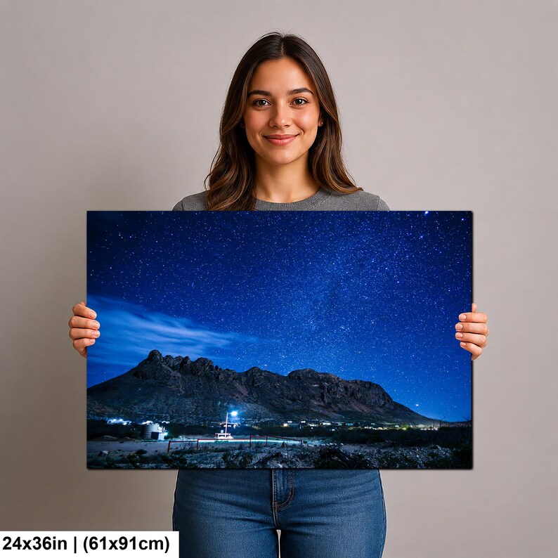 Puede incluir: Una impresi&oacute;n de arte mural rectangular que mide 61x91cm, con un paisaje nocturno de una cadena monta&ntilde;osa oscura bajo un cielo estrellado azul profundo. Una peque&ntilde;a estructura iluminada se encuentra en la base de las monta&ntilde;as, contrastando con el terreno oscuro.