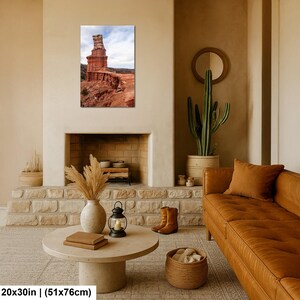 May include: A rectangular wall art print featuring a tall, weathered red sandstone rock formation under a cloudy sky. The print measures 20 inches by 30 inches and displays a desert landscape with layered geological textures and earthy tones.