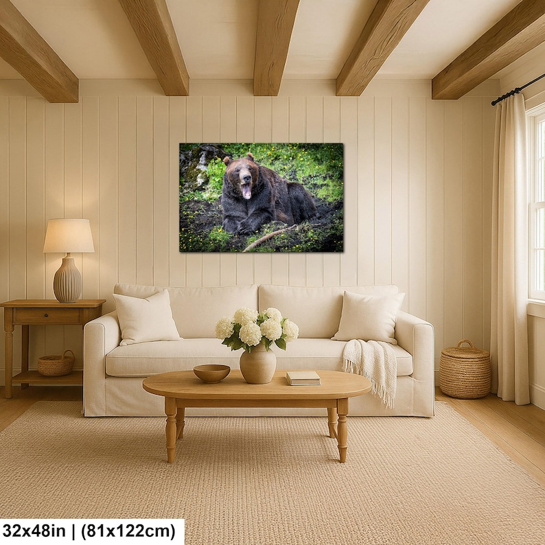 May include: A rectangular wall art print featuring a brown bear with its mouth open, resting in a lush green meadow filled with small yellow flowers. The artwork is displayed above a beige sofa in a living room, measuring 32 inches by 48 inches.