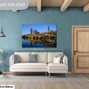 May include: A rectangular wall art print featuring a cityscape with a bridge and its reflection in the water, displayed above a cream-colored sectional sofa. The text "Livingroom size chart" appears at the top, and "40x60in | 101x152cm" at the bottom.