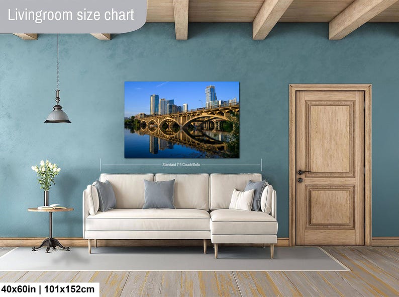 May include: A rectangular wall art print featuring a cityscape with a bridge and its reflection in the water, displayed above a cream-colored sectional sofa. The text "Livingroom size chart" appears at the top, and "40x60in | 101x152cm" at the bottom.