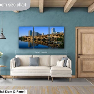 May include: A three-panel wall art set depicting a bridge and city skyline reflected in water, displayed above a white sectional sofa. The text "Livingroom size chart" appears at the top, and "36x72in | 91x183cm (3 Panel)" at the bottom.