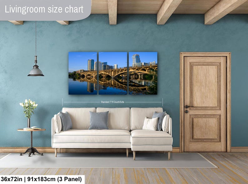 May include: A three-panel wall art set depicting a bridge and city skyline reflected in water, displayed above a white sectional sofa. The text "Livingroom size chart" appears at the top, and "36x72in | 91x183cm (3 Panel)" at the bottom.
