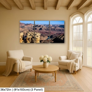 May include: A three-panel wall art set depicting a panoramic view of the Grand Canyon with layered rock formations in shades of brown, orange, and red under a clear blue sky. The total dimensions are 36 by 72 inches for the three panels.