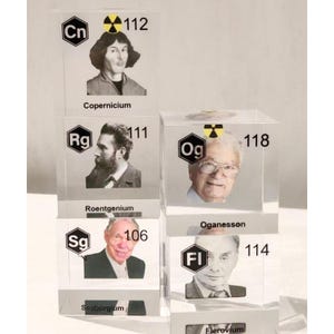 Puede incluir: Una colección de cubos de acrílico transparente con elementos de la tabla periódica. Cada cubo muestra un retrato en blanco y negro de un científico, un símbolo químico, un número atómico y un símbolo de radiación amarillo. Las etiquetas incluyen Copernicium, Roentgenium, Oganesson, Seaborgium y Flerovium.